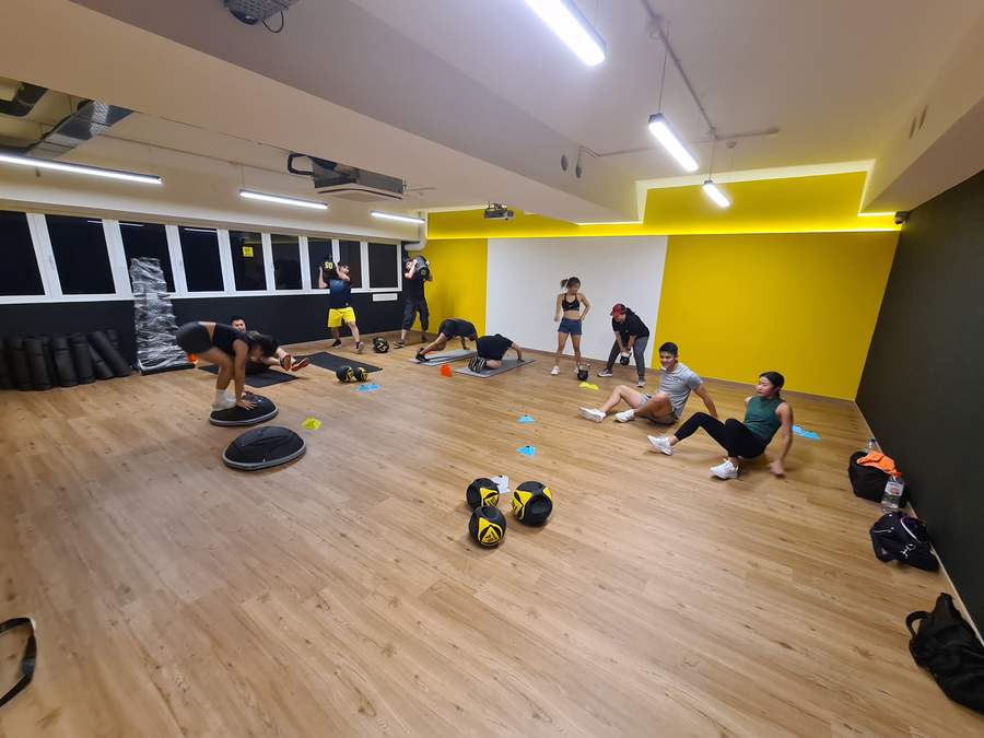 Members training in the GX studio with Bosu domes, medicine balls, sandbags and kettlebells under yellow and black walls