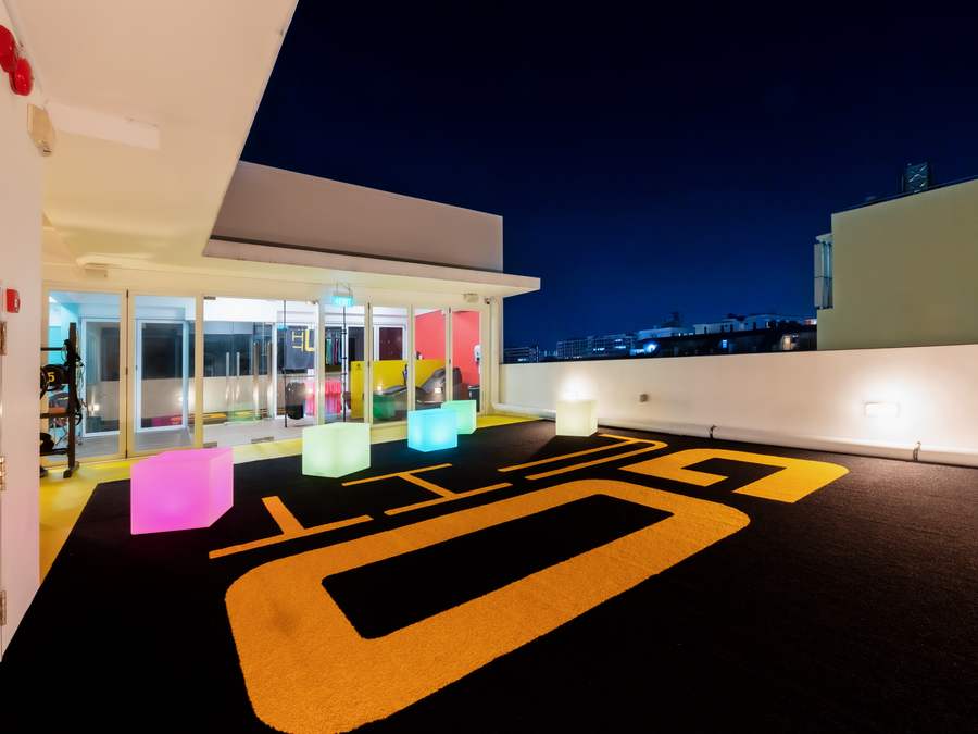 Rooftop training deck at night with the GoFit logo across black turf, glowing colour cubes and the Geylang skyline behind