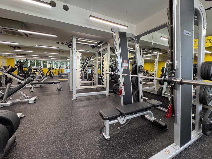 Smith machine and adjustable bench beside squat racks, reflected in the mirrored wall