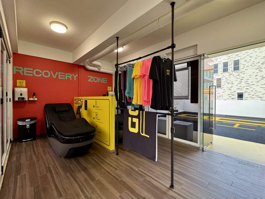 Recovery Zone with a HydroMassage lounger against a red wall and a rack of GoFit apparel beside the glass doors