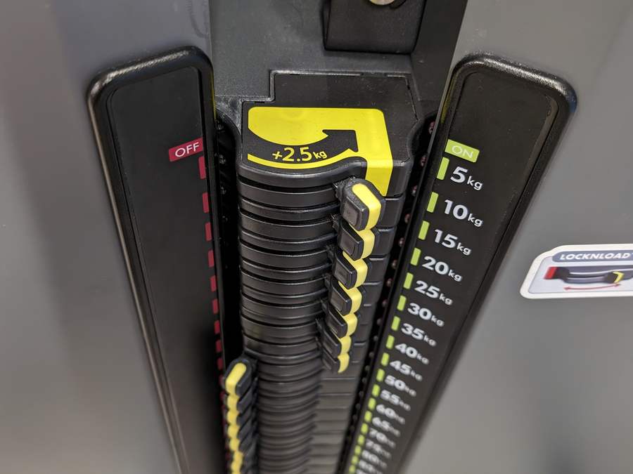 Close-up of a LockNLoad weight stack selector marked in five kilogram steps with a plus two point five kilogram adjuster